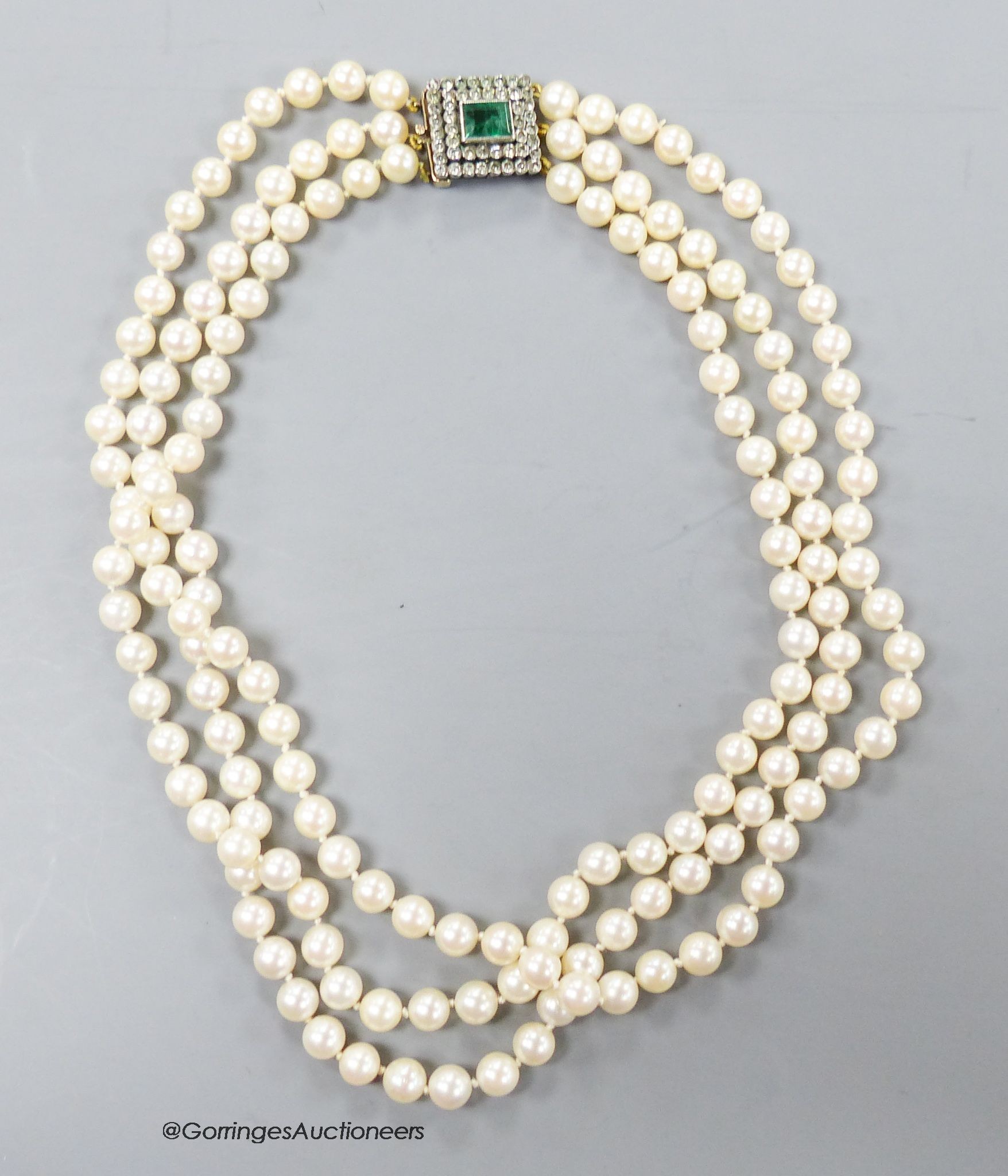 A triple strand cultured pearl set choker necklace, with two colour paste set yellow metal clasp, 42cm.